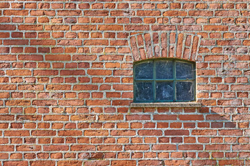 Small iron barn window recessed in a red brick wall. Spider web in the glazing
