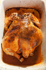 Baked whole chicken with herbs in white caserole