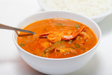 Thai red curry with shrimps, carrots, peppers and onion. Rice on background. Horizontal shot. Close up