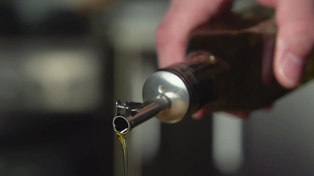 SLOW: A cook pours olive oil from oil bottle on a kitchen