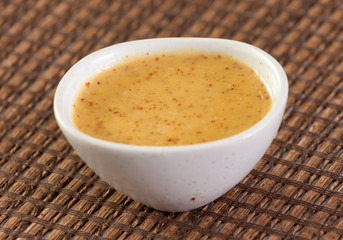 Close up of mustard sauce in white bowl over wooden surface.