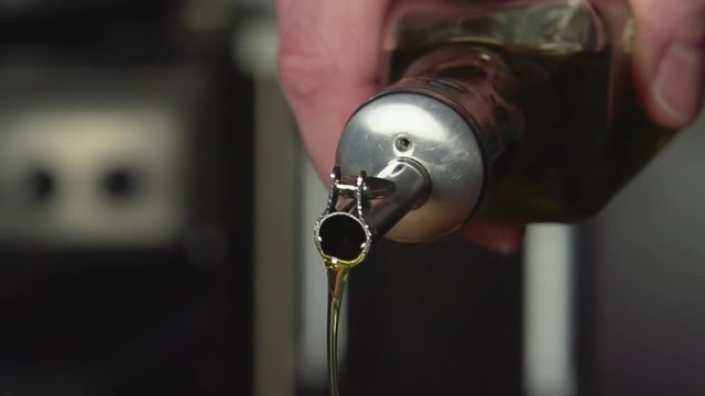 SLOW-CLOSE UP: A cook pours olive oil from oil bottle on a kitchen 