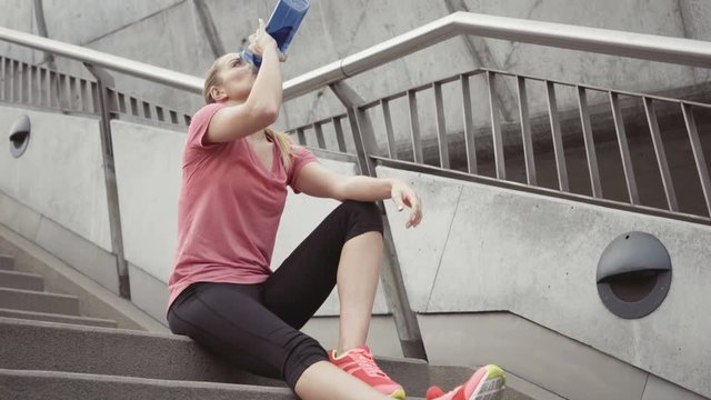 Young woman drinking water sitting on stairs after running exercise