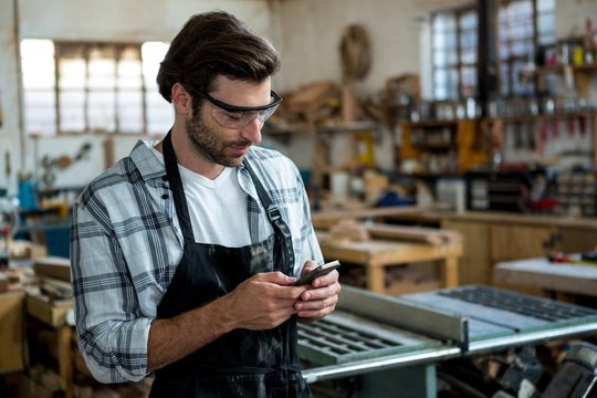 Carpenter texting someone and wearing protective glasses
