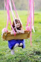baby girl in a blue dress riding on a swing against the backdrop