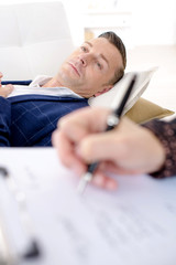 Man laying on couch, woman taking notes