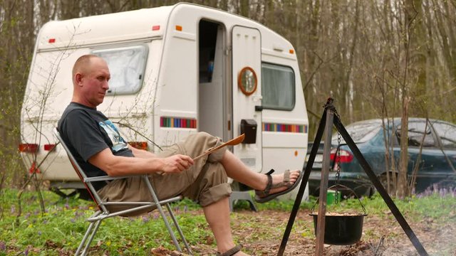 4K shot. Happy man in Life outdoors in  caravan, trailer. Cooking in wood