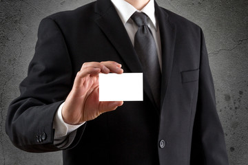 Mann im Anzug hält leere Visitenkarte vor dunkler Wand