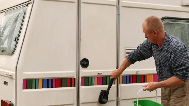 4K. Adult man washes  trailer, caravan  in  wood.