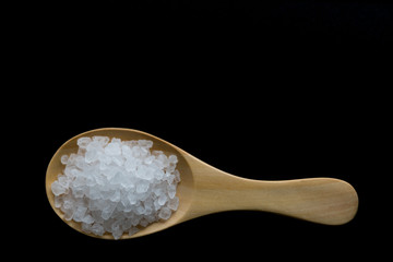 white crystals sea salt on wooden spoon on black background, top view