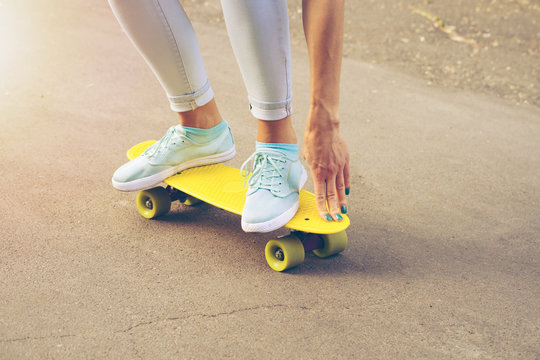 Girl rides on the road on a plastic skateboard in the sunlight