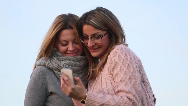 Two false blond girls taking selfie photo and laughing and giving five looking at the result. Outdoors