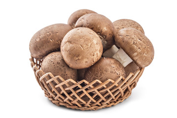 Fresh raw brown champignons mushrooms in woven basket on a white background