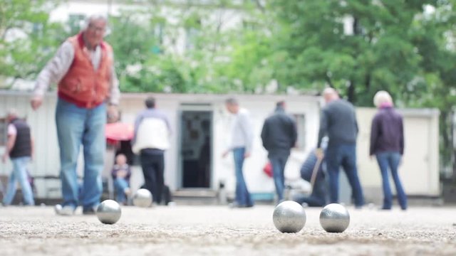 Seniors Playing Petanque in the Boules Court. Pétanque is a form of boules where the goal is to throw steel balls as close as possible to a small wooden ball called a cochonnet.
