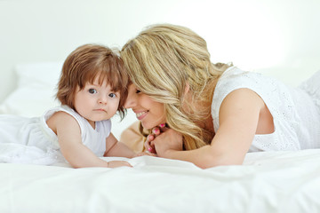 Happy mother with her funny baby on the bedroom