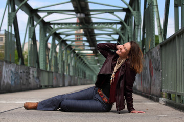 Beautiful brunette woman with leather jacket sitting on a bridge with graffiti
