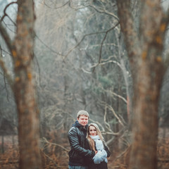 Young couple spend a weekend or holiday in park or pine forest. Against backdrop of mist or fog. Family values, spending time together, youth. Hug and kiss each other. Woman in white gloves