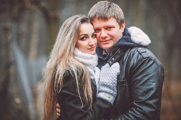 Young couple spend a weekend or holiday in park or pine forest. Against backdrop of mist or fog. Family values, spending time together, youth. Hug and kiss each other. Woman in white gloves