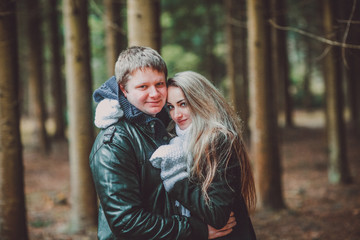 happy young loving couple in black leather jackets on the walk in pine forest. Woman in white gloves