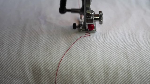 Sewing machine making line close up. Background white cloth and red thread.