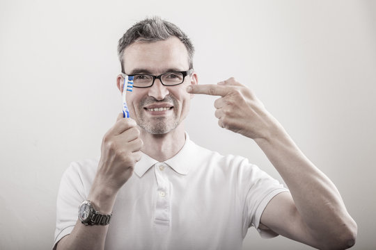 Zahnarzt zeigt mit dem Zeigefinger auf eine blau weisse Zahnb&uuml;rste