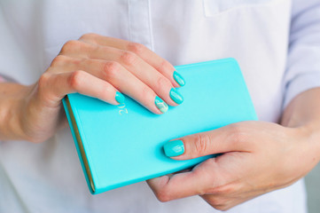 Closeup woman hands with elegant turquoise manicure holding blue diary