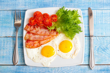 American Breakfast fried Eggs and bacon with tomato and lettuce on a wooden background 