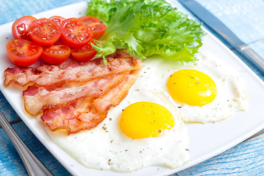 American Breakfast fried Eggs and bacon with tomato and lettuce on a wooden background 