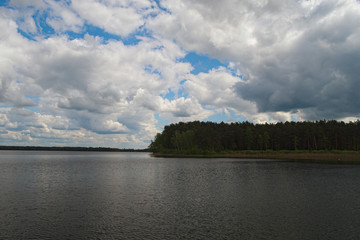 Scenic lake and forest.White clouds of different shapes are closing blue sky and sun (Pisochne ozero, Ukraine)