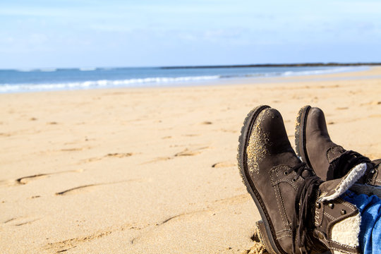 Füße in braunen Stiefeln an einem Strand an der an der Küste des leuchtend blauen Atlantik © GinaKoch