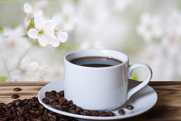 Coffee beans and coffee in white cup on wooden table opposite a
