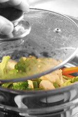 Steaming vegetables / Cooking vegetables in a steamer. Man removing lid.