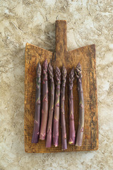 Fresh uncooked purple asparagus stalks on wooden board