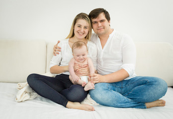 Happy young family posing with baby son on bed