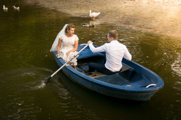 Fototapeta na wymiar Newly married couple riding on rowing boat on lake