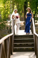 Beautiful bride posing with bridesmaid on wooden bridge