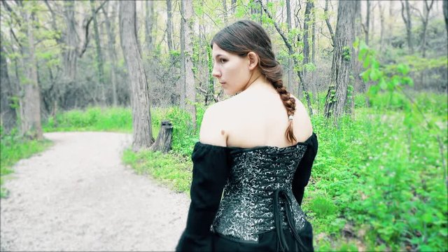 Young renaissance woman walking down path in forest on sunny day.