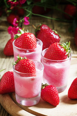 Pink granita with strawberries in a glass, old wooden background