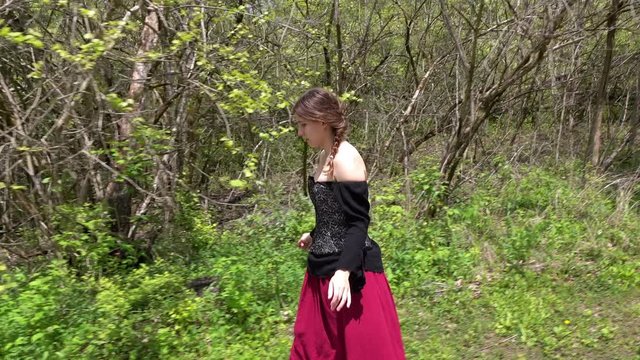 Young and free spirited renaissance woman walking near trees of forest.