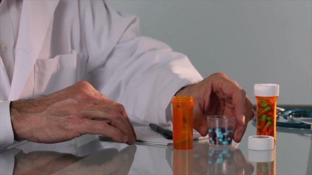 A pharmacist or doctor writes something on a prescription pad then pour some colorful caplets into a pill container.