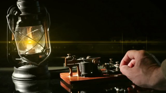 The flame from an oil latern throws a lens flare across a telegrapher sending a telegraph message.