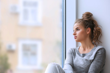 Fototapeta premium Beautiful young woman sitting on windowsill