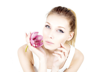 Portrait of woman with permanent make up holding pink flower and touching cheek.