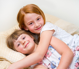 Two happy little girl hugging in the bed