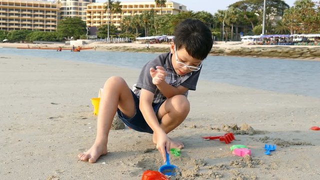 Asian Boy Plays In The Sand On Beach With Sand Toys
