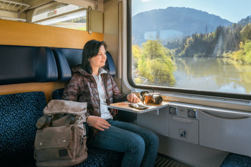 Woman traveler riding the train and listening to music on headphones lying on the table camera. Outside, a beautiful panorama. Traveling by train at the Alpine Railroad