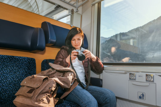 Girl riding on a train and watching pictures on the camera. Traveling by train at the Alpine Railroad