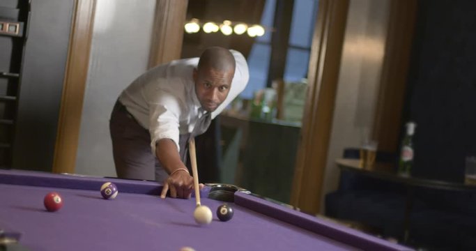 African American business man playing pool on a purple table in a bar lounge setting.  Focus on face and recorded in slow motion at 60fps.