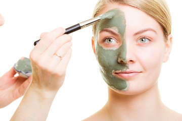 Cosmetician applying clay facial mask at woman face.