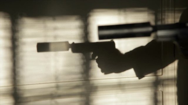The evening or morning sunlight through window blinds captures the silhouetted firing of a pistol with a suppressor attached to it. Blaze and smoke added to gun action in After Affects.